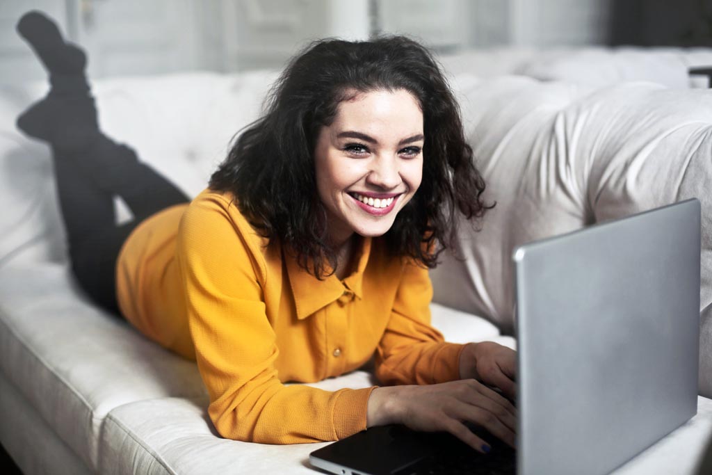 young woman in yellow jumper on sofa with computer